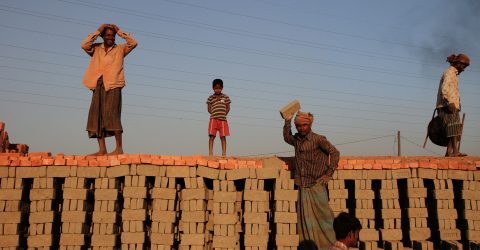 Workers standing on the rows of stacked raw bricks at the edge of the brick kiln