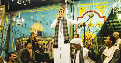 A group of people wearing traditional clothes from the Egyptian culture listening to the singer